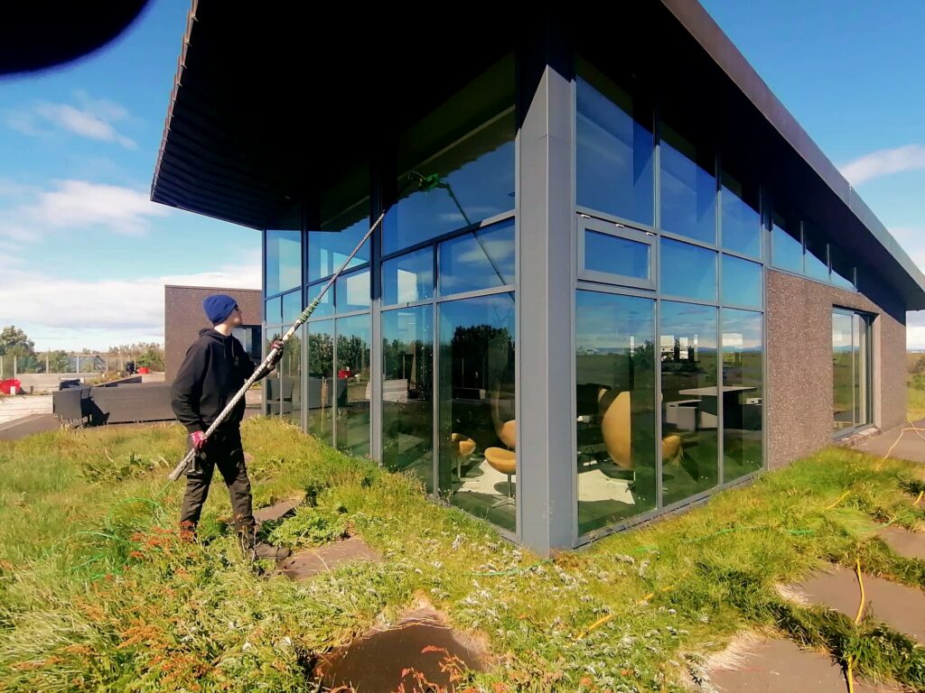Starfsmaður að þvo stóra glugga utan frá með vatnsskafti.