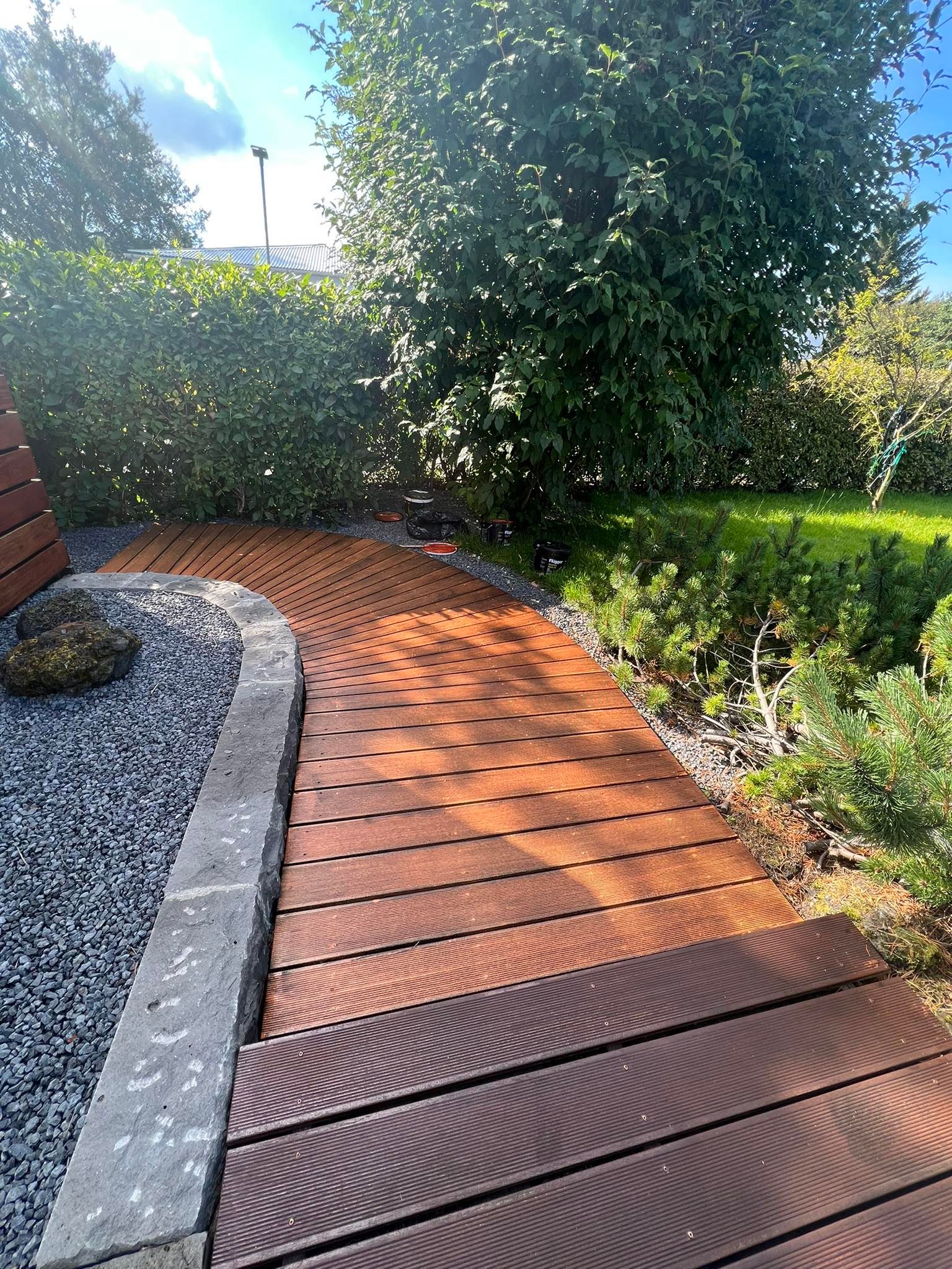 Sveigður timburstígur í blómlegum garði hjá Garðaþjónustu Sigurjóns.