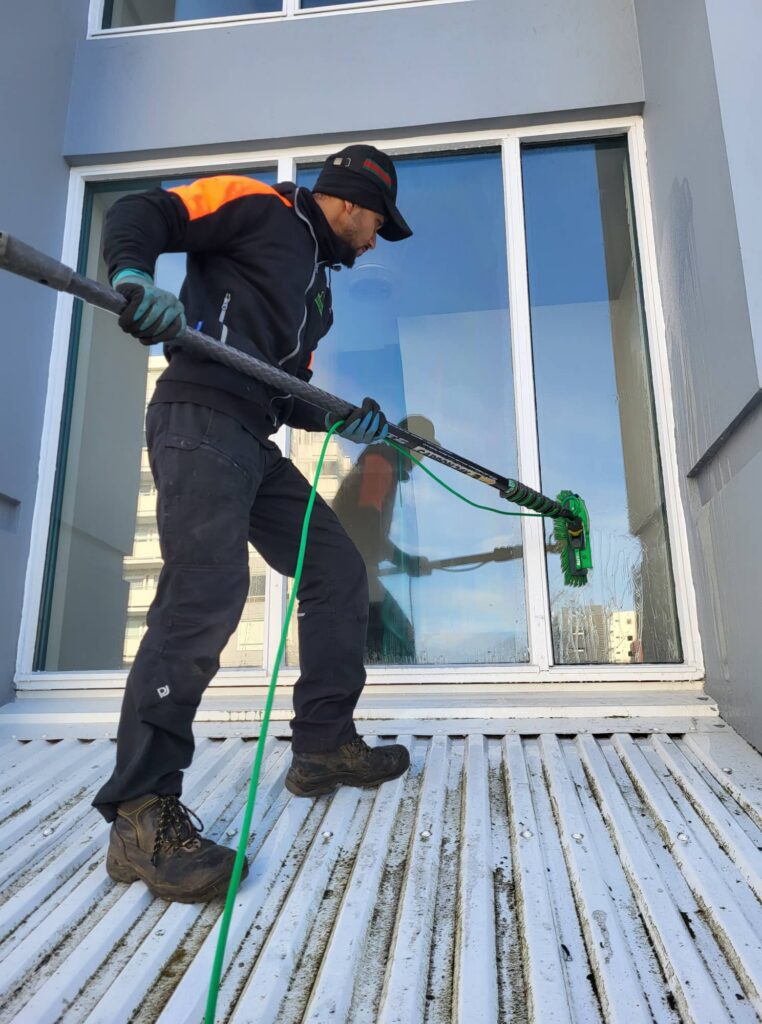 Öryggið á oddinum við gluggaþvott á þaki. Starfsmaður notar langt skaft til að ná til glugga sem erfitt er að komast að.