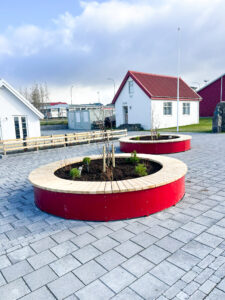Hringlaga rauð blómabeð og gráar hellur á útisvæði.