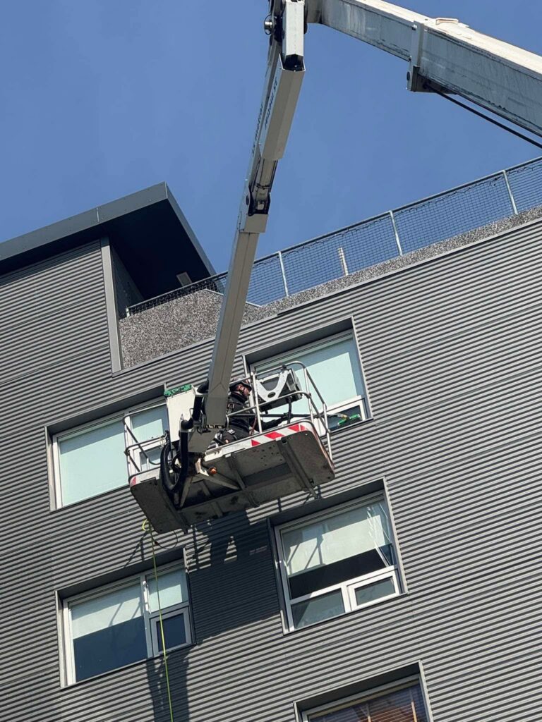 Gluggaþvottur í mikilli hæð með körfubíl. Þrif á gluggum á atvinnuhúsnæði klæddu bárujárni.