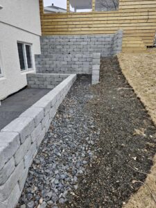 Frágangur á beðum og stétt meðfram húsvegg þar sem unnið er með grjót og timbur.