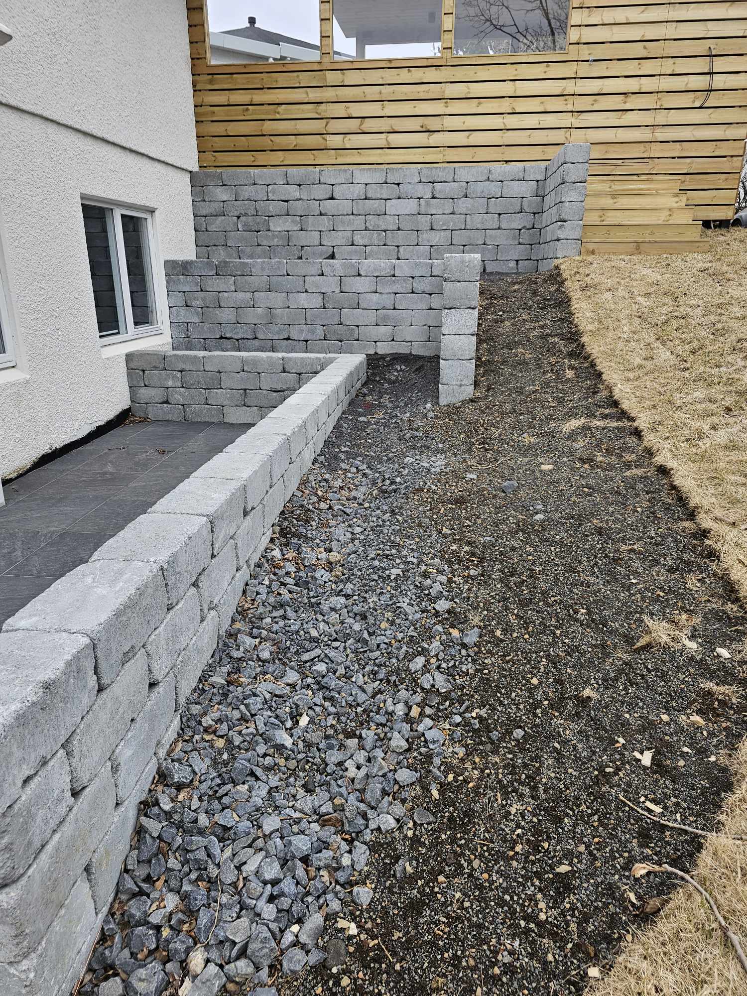 Frágangur á beðum og stétt meðfram húsvegg þar sem unnið er með grjót og timbur.