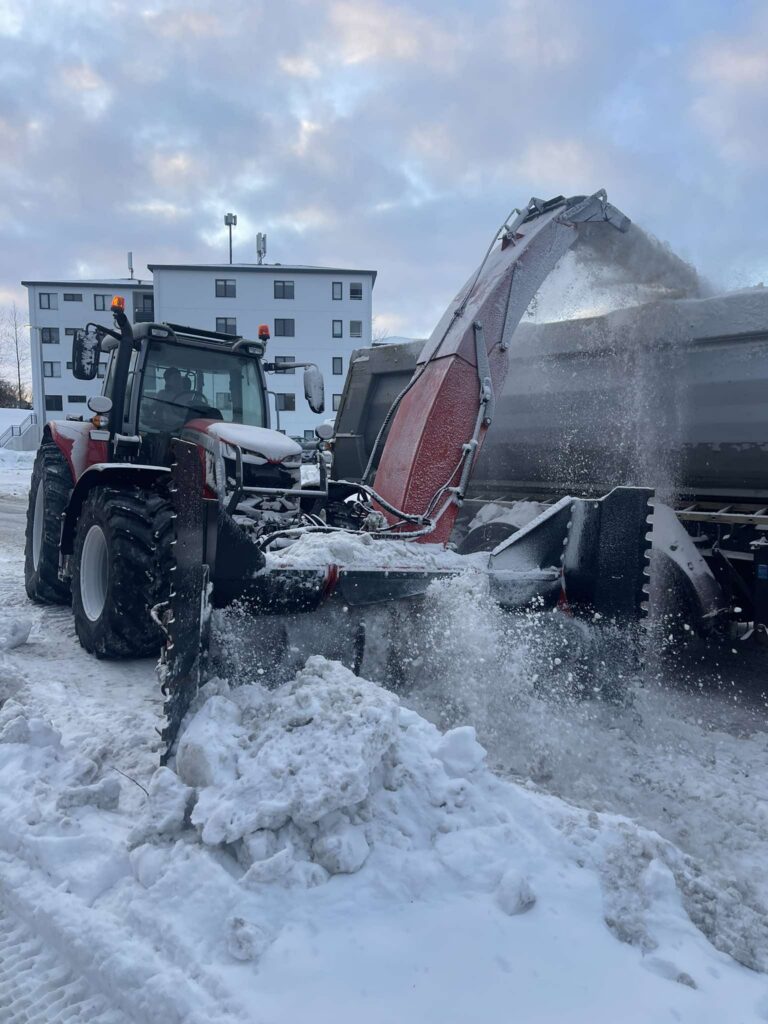 Dráttarvél með öflugum snjóblásara að blása snjó upp á vörubílspall til brottaksturs.