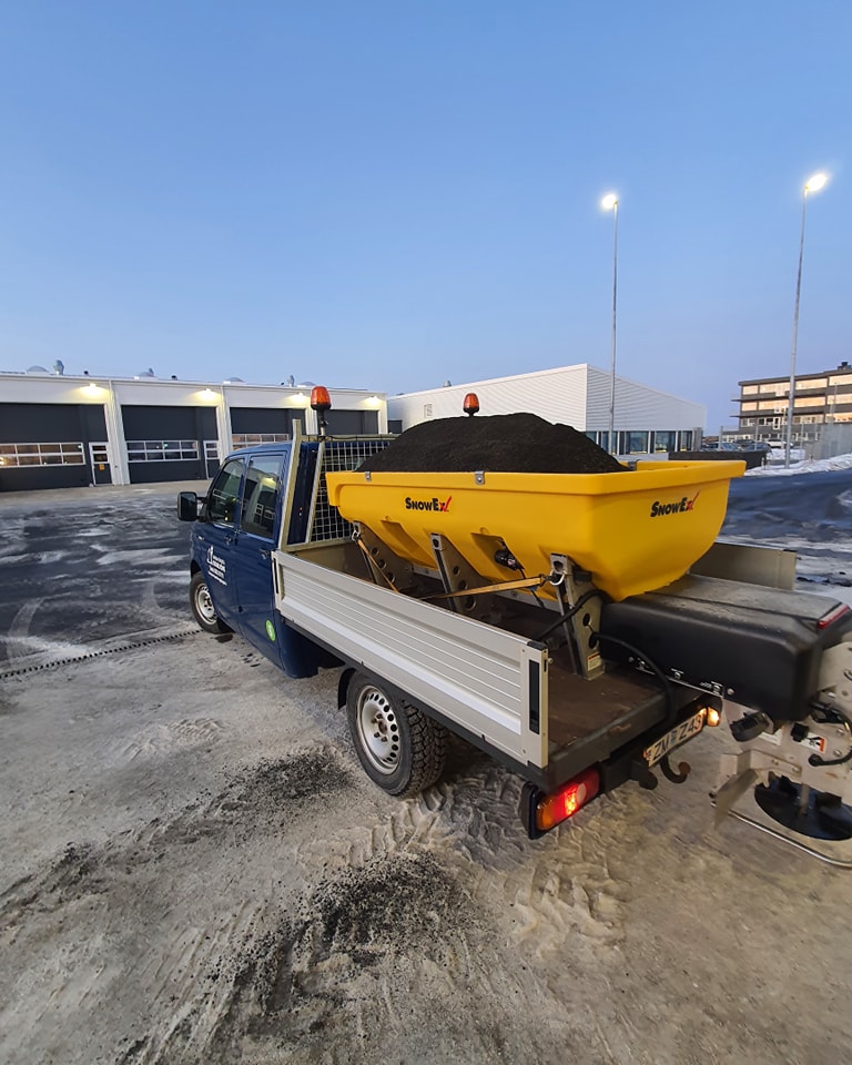 Pallbíll með gulri SnowEx salt- og sanddreifivél á pallinum. Tækjabúnaður klár í hálkuvarnir.