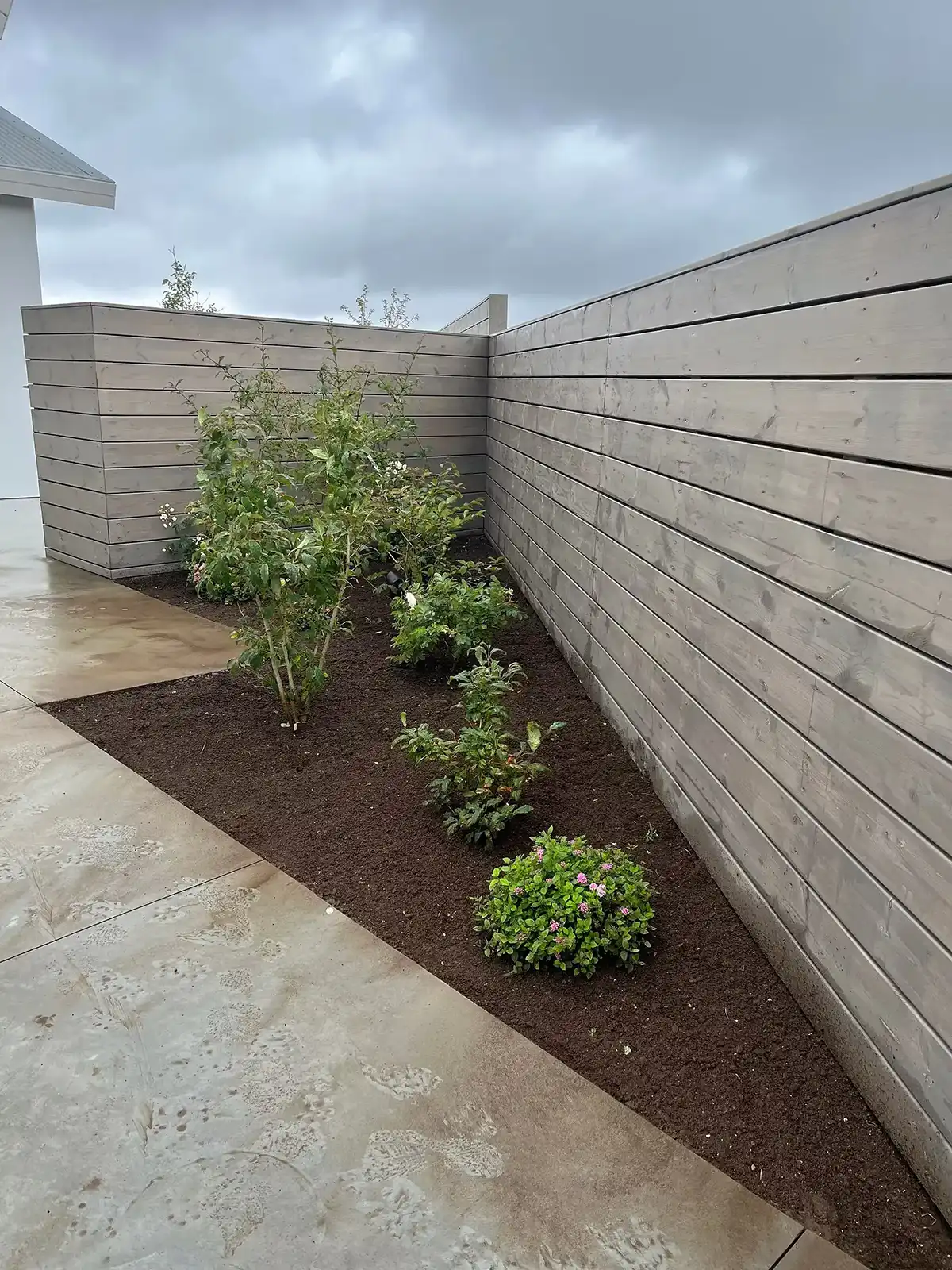 Garðahreinsun og beðahreinsun við nútímalegan timburvegg með nýrri mold.