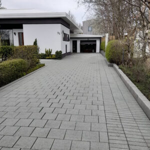 Grá hellulögð innkeyrsla með hita í jörðu og snyrtilegum frágangi við íbúðarhús.