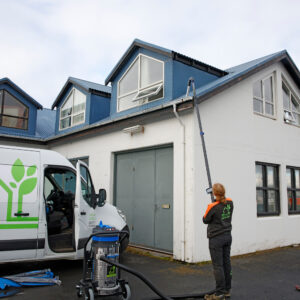 Starfsmaður Garðaþjónustu Sigurjóns að hreinsa þakrennur á tvílyftu húsi með sérhæfðum SkyVac ryksugubúnaði frá jörðu niðri.