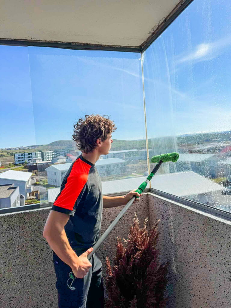 Sólskin og gluggaþvottur. Starfsmaður að gera svalalokun glæra og fína fyrir sumarið.