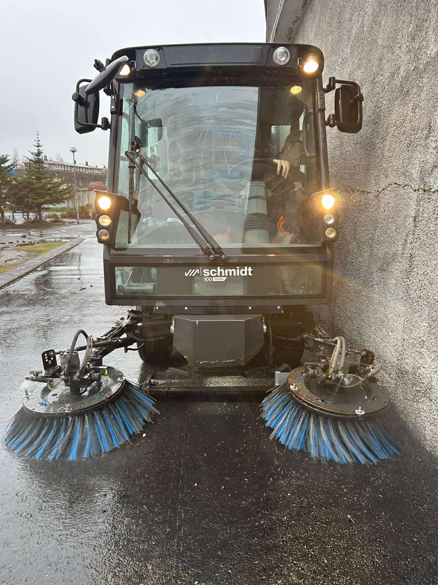 Nærmynd af götusópara með burstana á fullu að þrífa blauta stétt. Öflug vélahreinsun.