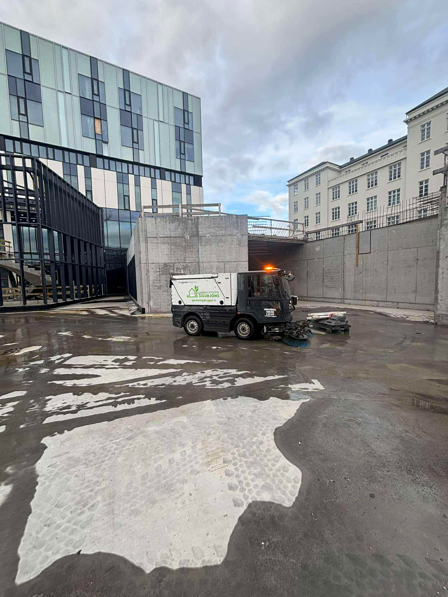 Götusópari að þrífa steypt plan við nýlega byggingu. Hreinsun á byggingarsvæðum og stéttum.