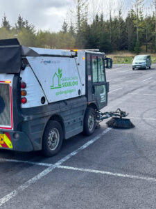 Götusópari að hreinsa sand og ryk af bílaplani. Vélasópun tryggir hreint yfirborð.