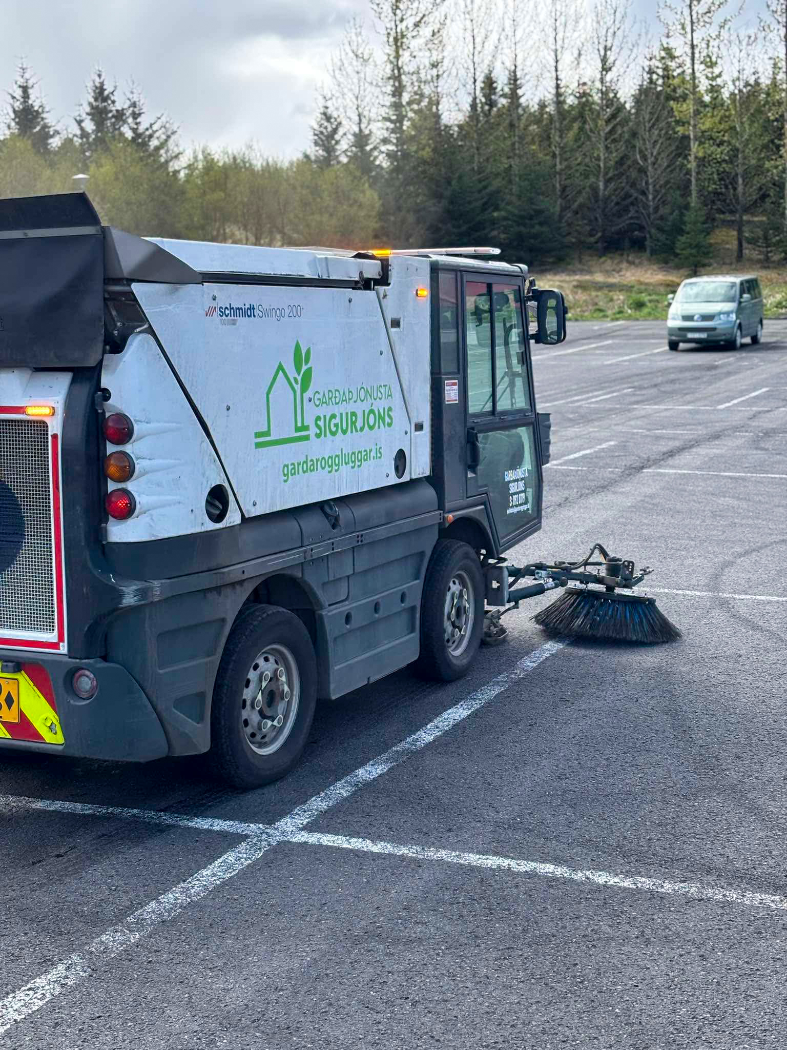 Götusópari að hreinsa sand og ryk af bílaplani. Vélasópun tryggir hreint yfirborð.
