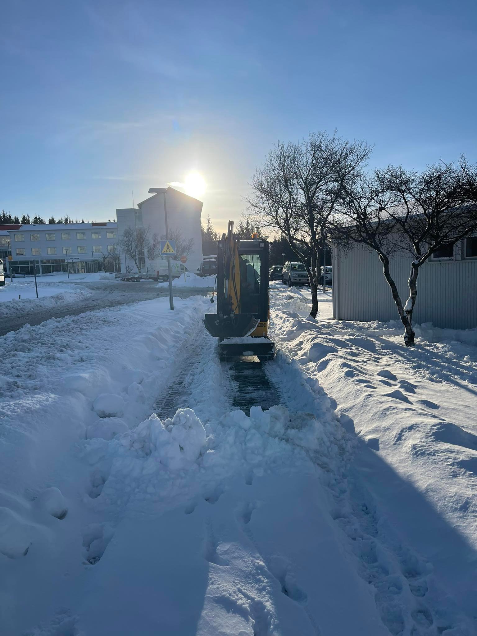 Snjómokstur á göngustíg. Lítil vinnuvél ryður leiðina fyrir gangandi vegfarendur.