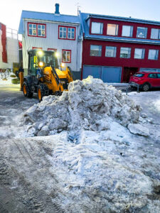 JCB traktorsgrafa að ryðja snjó í stóran haug í íbúðahverfi í Reykjavík.