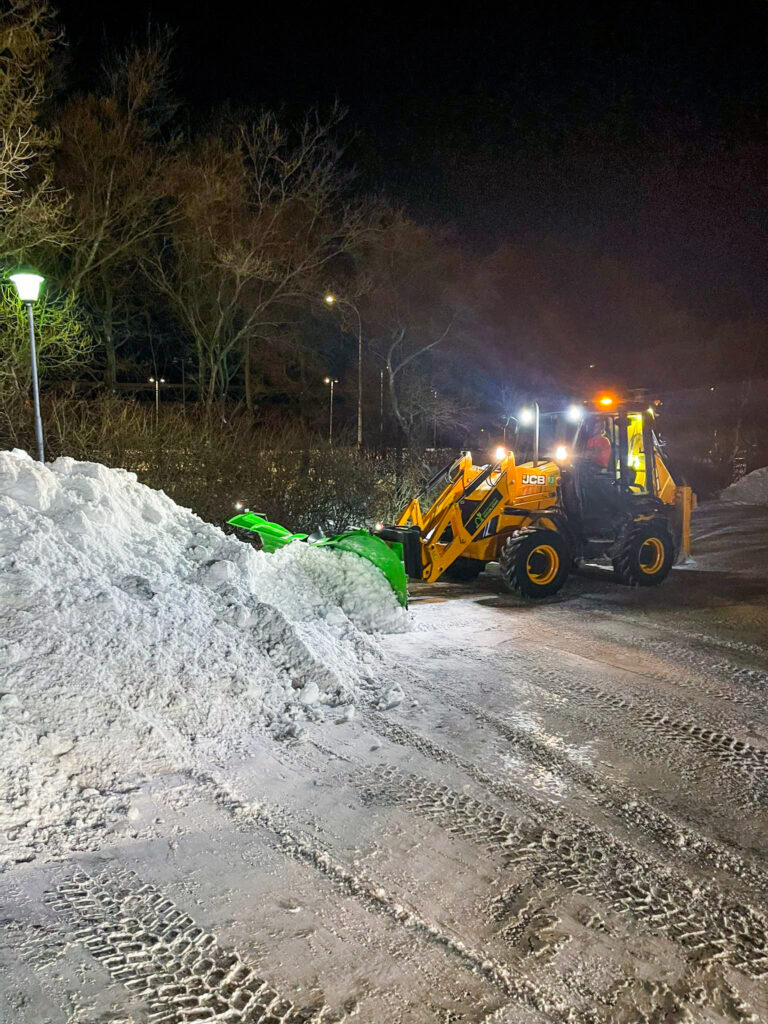 Snjómokstur að næturlagi. Traktorsgrafa að ryðja bílaplan og tryggja aðgengi fyrir morguninn.