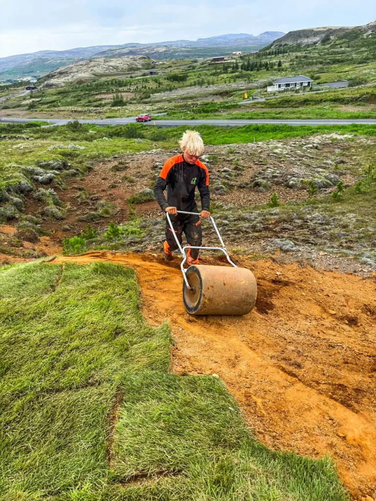 Starfsmaður að valta nýlagðar þökur með handvaltara til að tryggja góða festu við jarðveg.