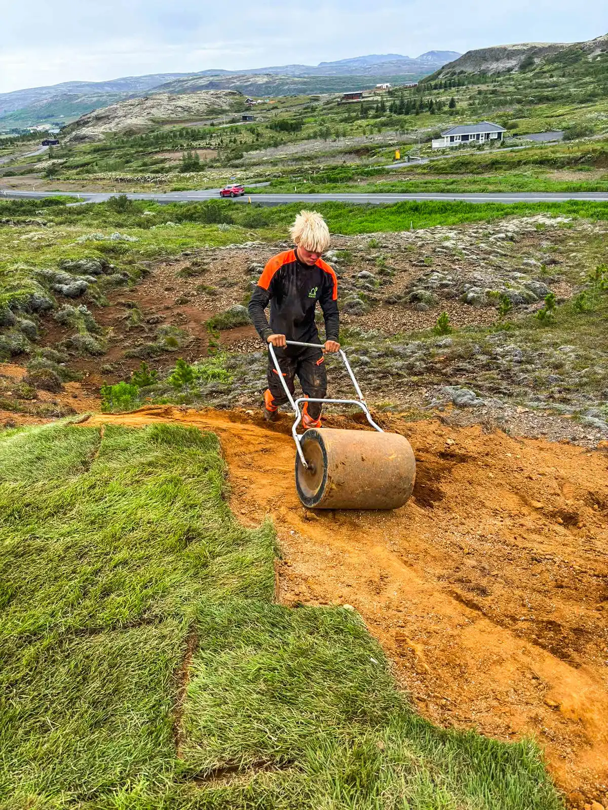 Starfsmaður að valta nýlagðar þökur með handvaltara til að tryggja góða festu við jarðveg.