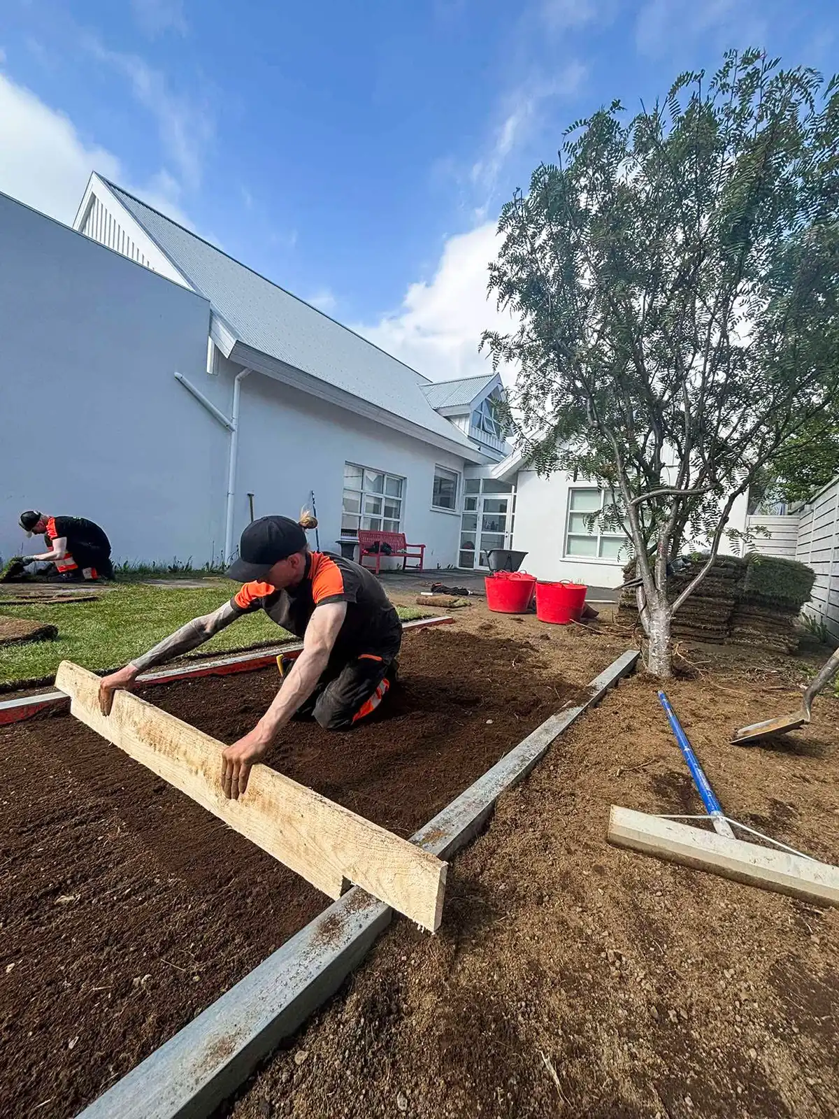 Starfsmaður að jafna jarðveg og undirbúa undirlaag fyrir þökulagningu við íbúðarhús.