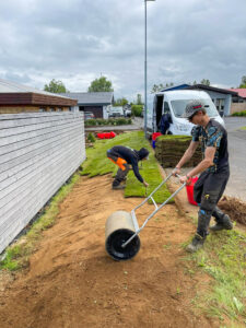 Starfsmaður að notast við tromlu til að valta nýlagða grasflöt eftir þökulagningu.