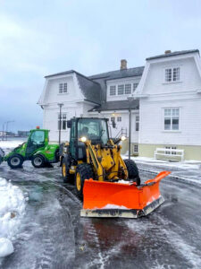 Gul CAT hjólaskófla með appelsínugula V-snjótennu og græn Avant vinnuvél fyrir framan Höfða.