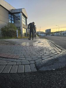 Starfsmaður að háþrýstiþvo hellulögn við atvinnuhúsnæði