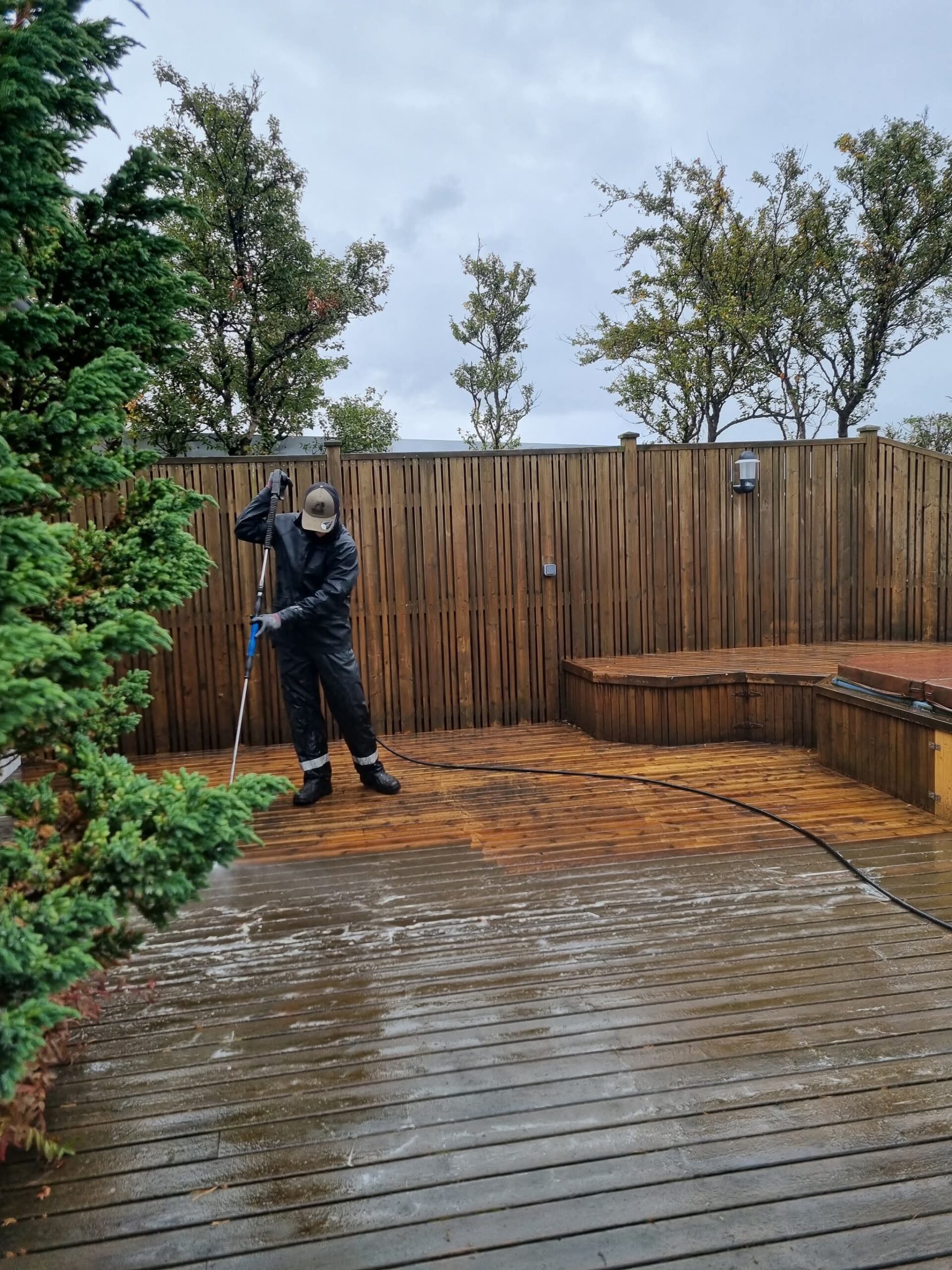 Starfsmaður að spúla og hreinsa pall í kringum heitan pott og skjólvegg