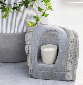 Útskorin steinlukt með hvítu kerti, stillt upp við hliðina á potti með bergfléttu. Skapar hlýlega stemningu.