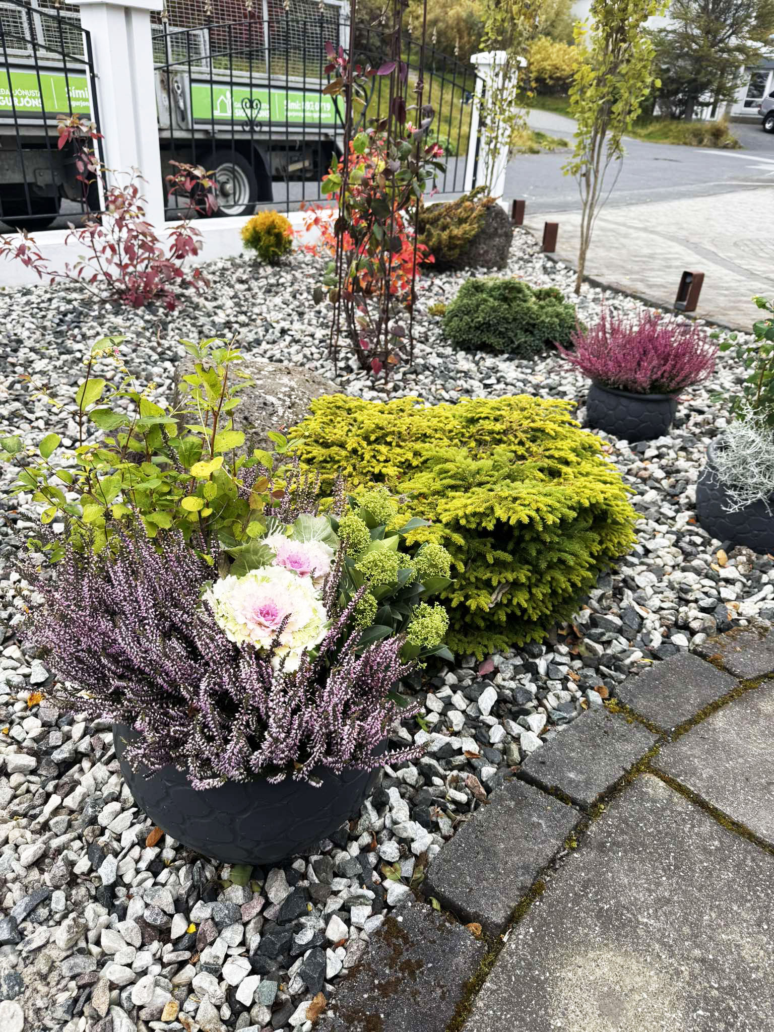 Falleg haustskreyting í potti með skrautkáli og lyngi. Snyrtilegt beð með möl og bíll Garðaþjónustu Sigurjóns í bakgrunni.