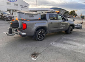 Grár VW Amarok pallbíll búinn Hilltip snjóplóg og saltdreifara fyrir skilvirkan snjómokstur og hálkuvarnir.