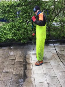 Starfsmaður í gulum galla að þrífa stétt með háþrýstidælu