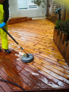 Starfsmaður að þrífa viðarpall með sérhæfðum pallabursta og háþrýstidælu