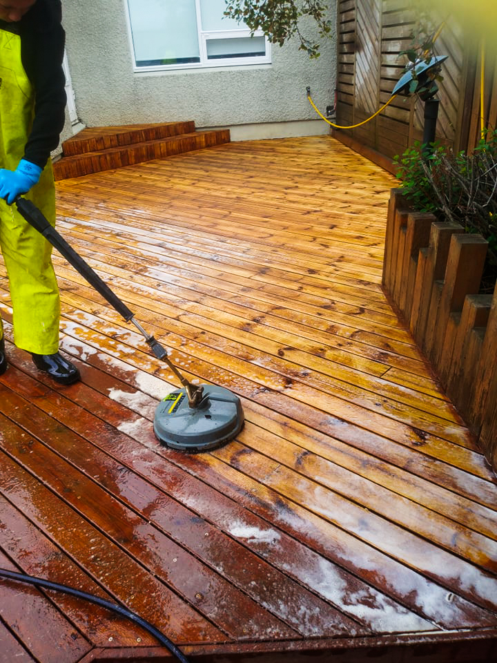 Starfsmaður að þrífa viðarpall með sérhæfðum pallabursta og háþrýstidælu